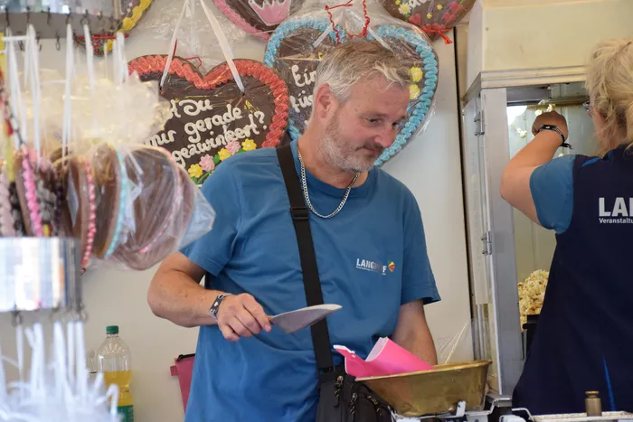 Ein Mann in einem blauen T-Shirt steht an einem Stand mit hängenden Lebkuchenherzen auf dem Bautz-Festival.