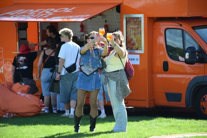 Zwei Frauen stoßen vor einem orangefarbenen Aperol Spritz Truck mit ihren Gläsern an.