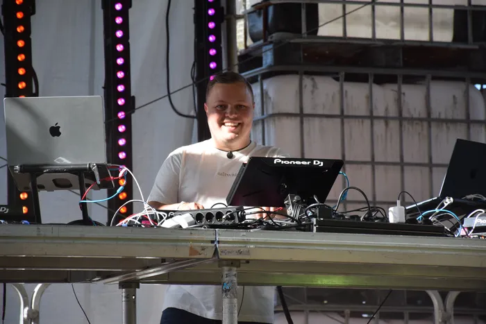 Ein lächelnder Mann steht hinter einem DJ-Pult mit Laptop und Pioneer DJ Controller auf dem Bautz-Festival.