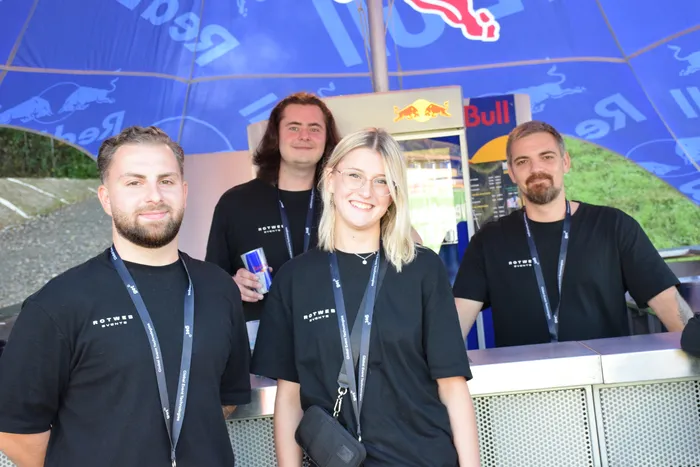 Vier Personen in schwarzen T-Shirts mit der Aufschrift „Rotweber Events“ stehen hinter einem Tresen unter einem blauen Red Bull Schirm auf dem Bautz-Festival.