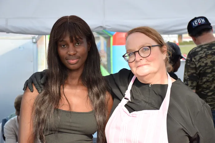 Eine junge Frau mit langen dunklen Haaren und eine ältere Frau mit Brille und rosa Schürze stehen eng beieinander auf dem Bautz-Festival.