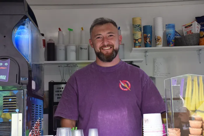 Ein lächelnder Mann mit Bart steht hinter der Theke eines Verkaufsstandes auf dem Bautz-Festival.