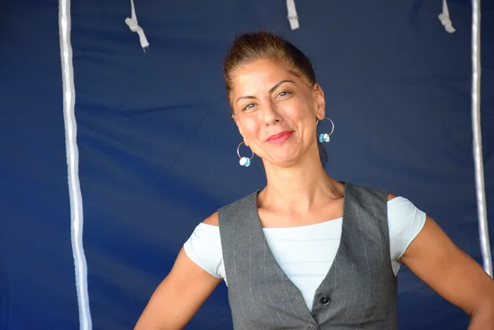 Eine lächelnde Frau in einer grauen Weste und einem hellblauen Shirt vor einem blauen Hintergrund beim Bautz-Festival.