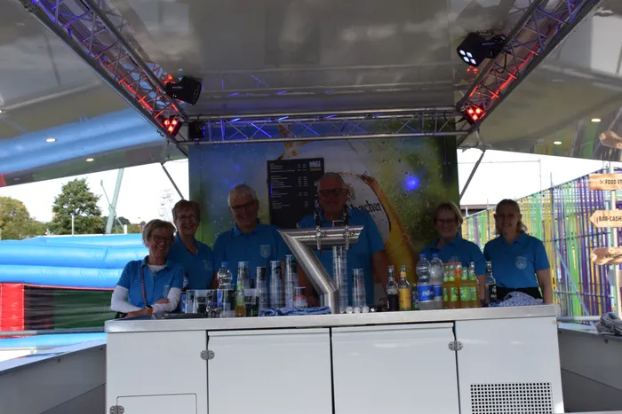 Sechs Personen in blauen Poloshirts stehen hinter einer weißen Bar mit verschiedenen Getränken auf dem Bautz-Festival.