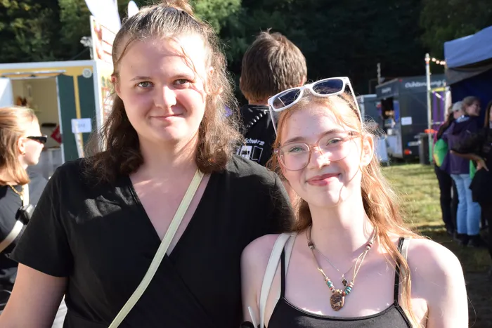 Zwei lächelnde junge Frauen auf dem Bautz-Festival vor Festivalständen und Menschen.