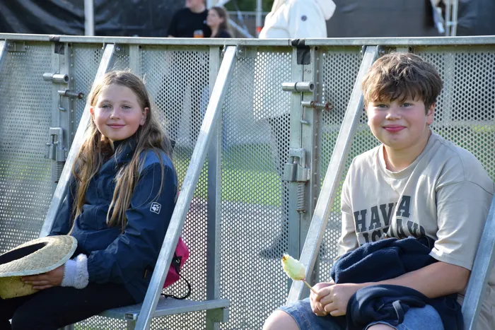 Ein Mädchen mit Strohhut und ein Junge mit einem Eis sitzen auf Metallgerüsten beim Bautz-Festival.