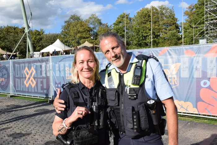 Zwei lächelnde Sicherheitskräfte in Uniform stehen vor einem Zaun auf dem Bautz-Festival.