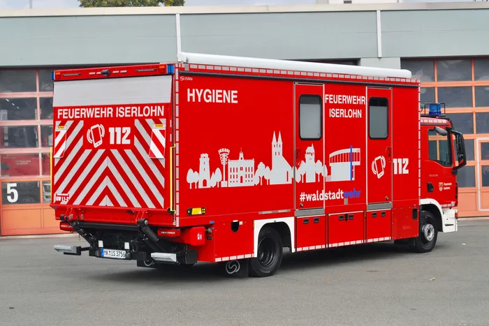 Rotes Feuerwehrfahrzeug der Feuerwehr Iserlohn mit der Aufschrift „HYGIENE“ und einer weißen Skyline-Grafik auf der Seite.