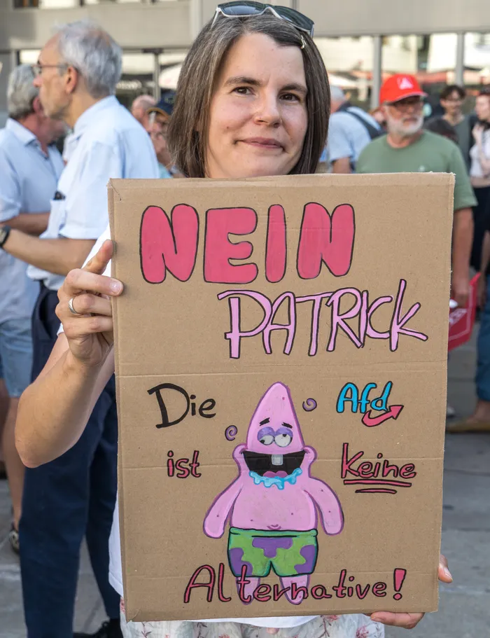 Eine Frau hält ein Pappschild mit der Aufschrift „NEIN PATRICK Die AfD ist keine Alternative!“ und einer Zeichnung von Patrick Star hoch.