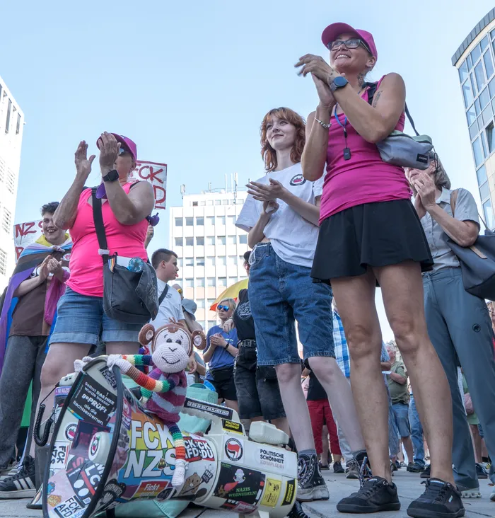 Menschen klatschen bei einer Kundgebung gegen Rechts. Im Vordergrund steht eine mit politischen Aufklebern wie „FCK NZS“ verzierte Trommel.