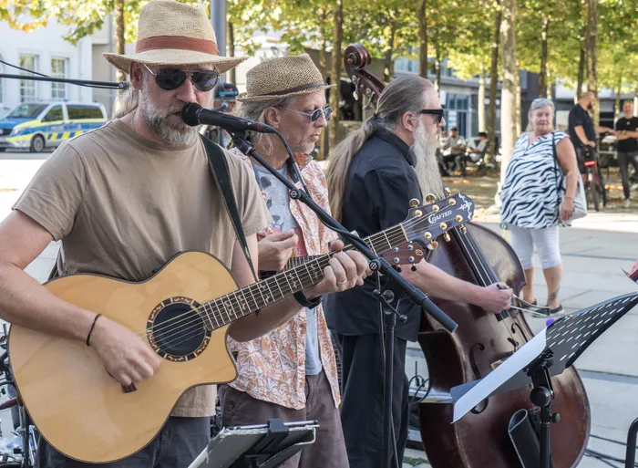 Drei Musiker des Stadtbild Orchesters spielen Akustikgitarre und Kontrabass im Freien.