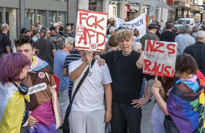 Demonstranten halten bei einer Kundgebung Schilder mit den Aufschriften „FCK AFD“ und „NZS RAUS!“ hoch.