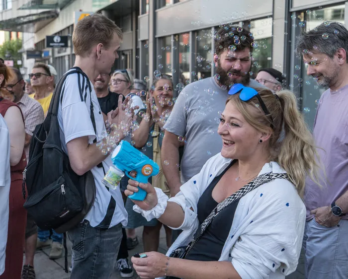 Eine lachende Frau bläst mit einer blauen Seifenblasenpistole Seifenblasen in eine Menschenmenge während einer Kundgebung.
