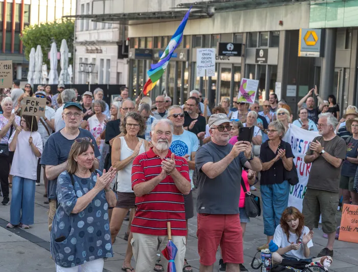 Menschen bei einer Kundgebung gegen die AfD in Lüdenscheid mit Protestschildern und einer Regenbogenfahne.