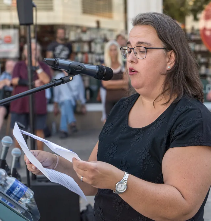 Julia Denker spricht bei einer Kundgebung in ein Mikrofon und hält ein Blatt Papier in den Händen.