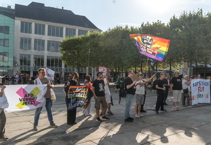 Demonstranten halten bei einer Kundgebung Banner mit der Aufschrift „AfD VERBOT JETZT“ und „kein mensch ist illegal“ sowie eine Regenbogenfahne hoch.