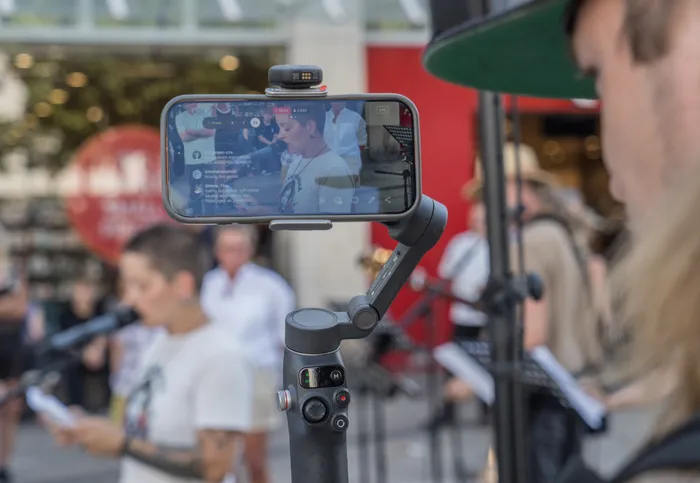 Ein Smartphone auf einem Gimbal zeigt auf seinem Display die Live-Übertragung der Ansprache von Carina Büdenbender.