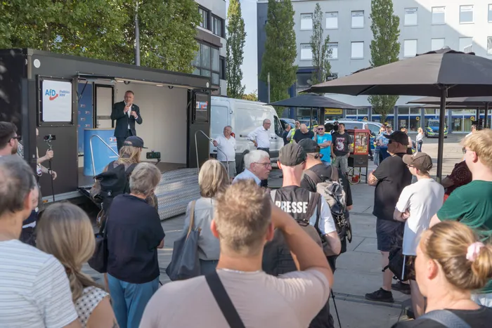 Ein Mann spricht von einer Plattform auf einem schwarzen LKW mit AfD-Logo zu einer Menschenmenge auf einem Platz.
