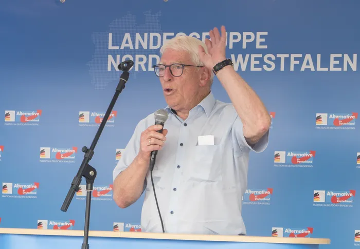 Otto Strauß spricht mit erhobener Hand in ein Mikrofon vor einem blauen Hintergrund der AfD Landesgruppe Nordrhein-Westfalen.