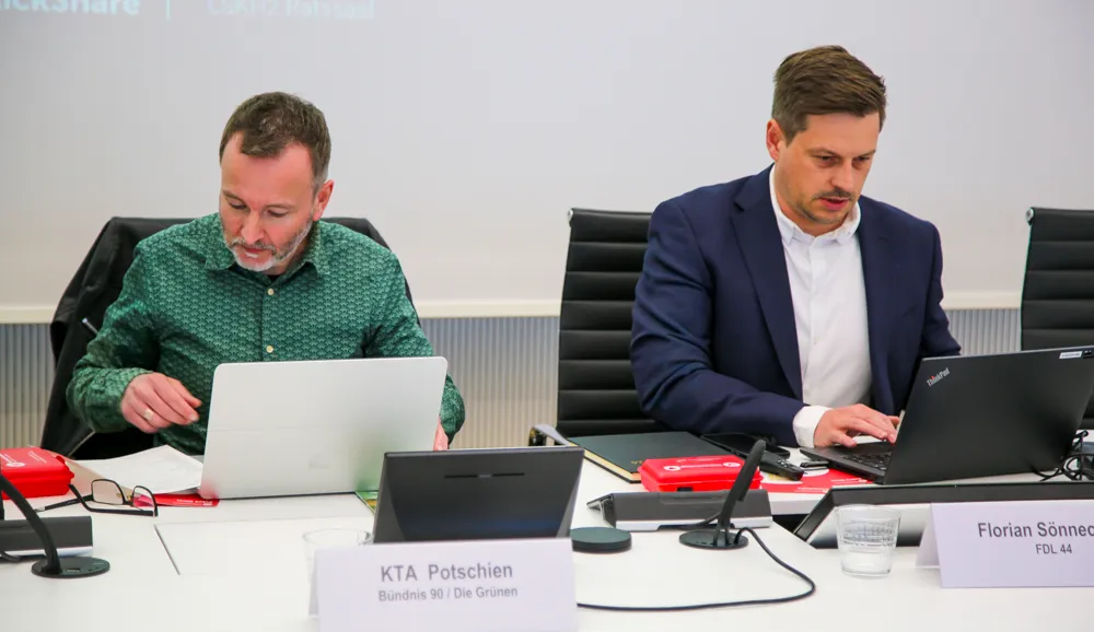 Zwei Männer sitzen an einem Konferenztisch und tippen auf Laptops. Links Denis Potschien, rechts Florian Sönnecken, beide konzentriert bei der Arbeit.