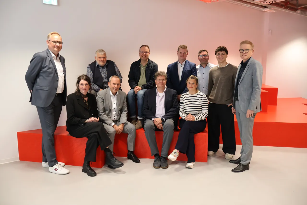 Eine Gruppe von zehn Personen sitzt und steht vor einem roten Hintergrund. Sie lächeln in die Kamera und bilden den neuen b.invest-Beirat.