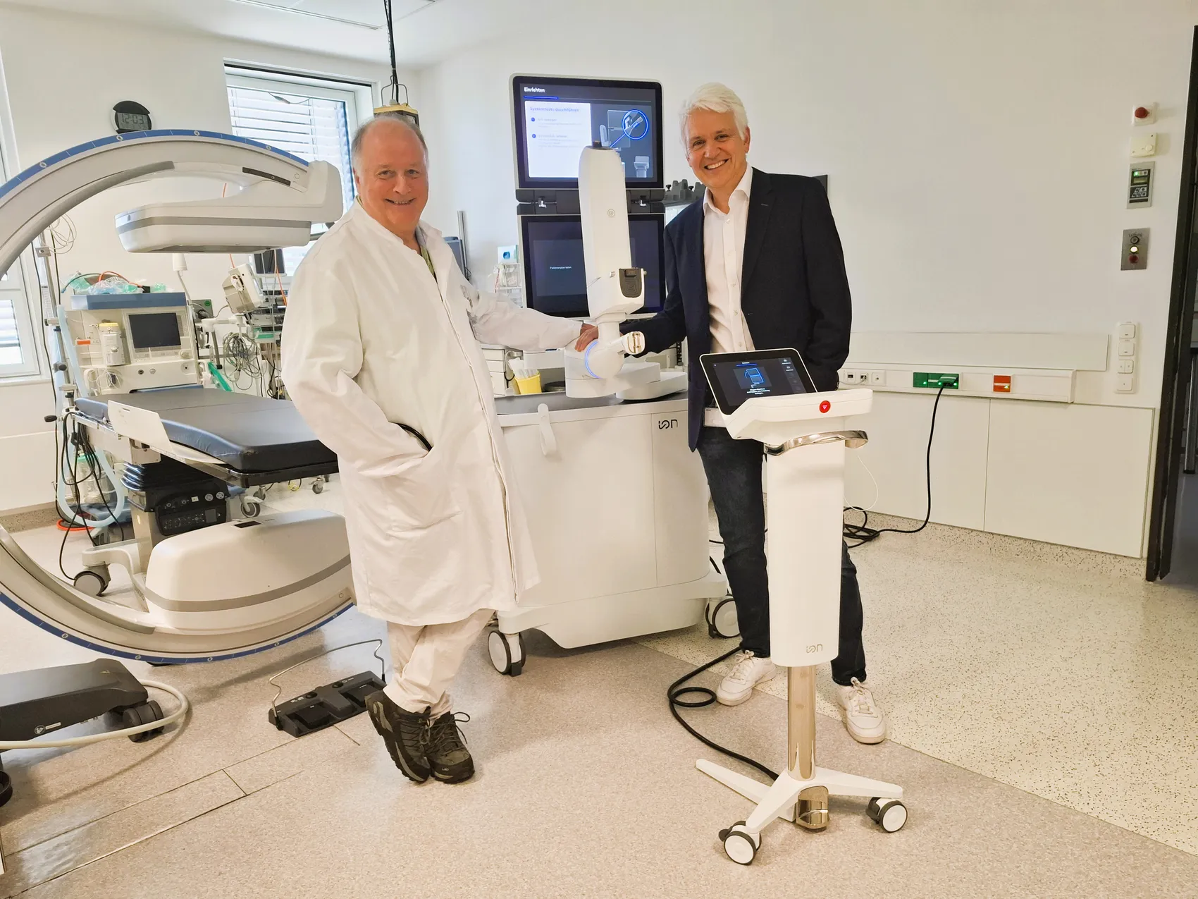Dr. Wolfgang Hohenforst-Schmidt im Laborkittel und Dr. Thorsten Kehe im Anzug stehen lächelnd neben einem weißen robotergestützten Bronchoskopie-System.