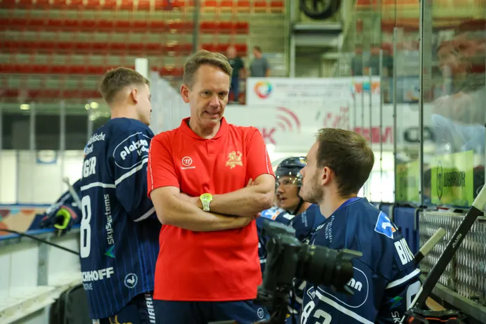 Mannschaftsarzt Dr. Jochen Veit im roten Poloshirt im Gespräch mit dem Eishockeyspieler Kevin Bicker in blauem Trikot in einer Eishalle.