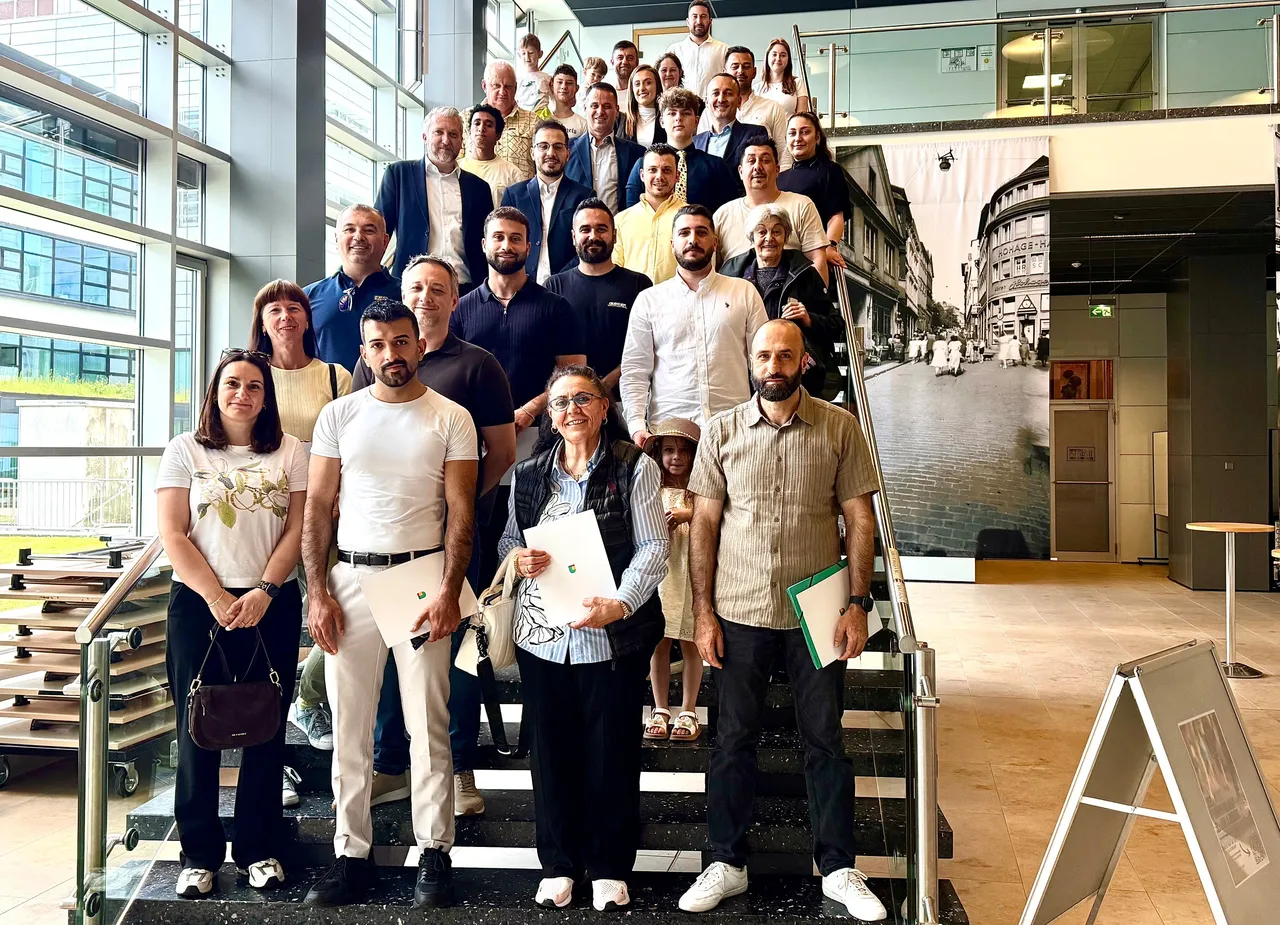 Eine Gruppe von 44 Menschen steht auf einer Treppe vor einer Fotografie eines Fachwerkhauses. Bürgermeister Sebastian Wagemeyer ist in der vorderen Reihe zu sehen und gratuliert den Neu-Bürgern.