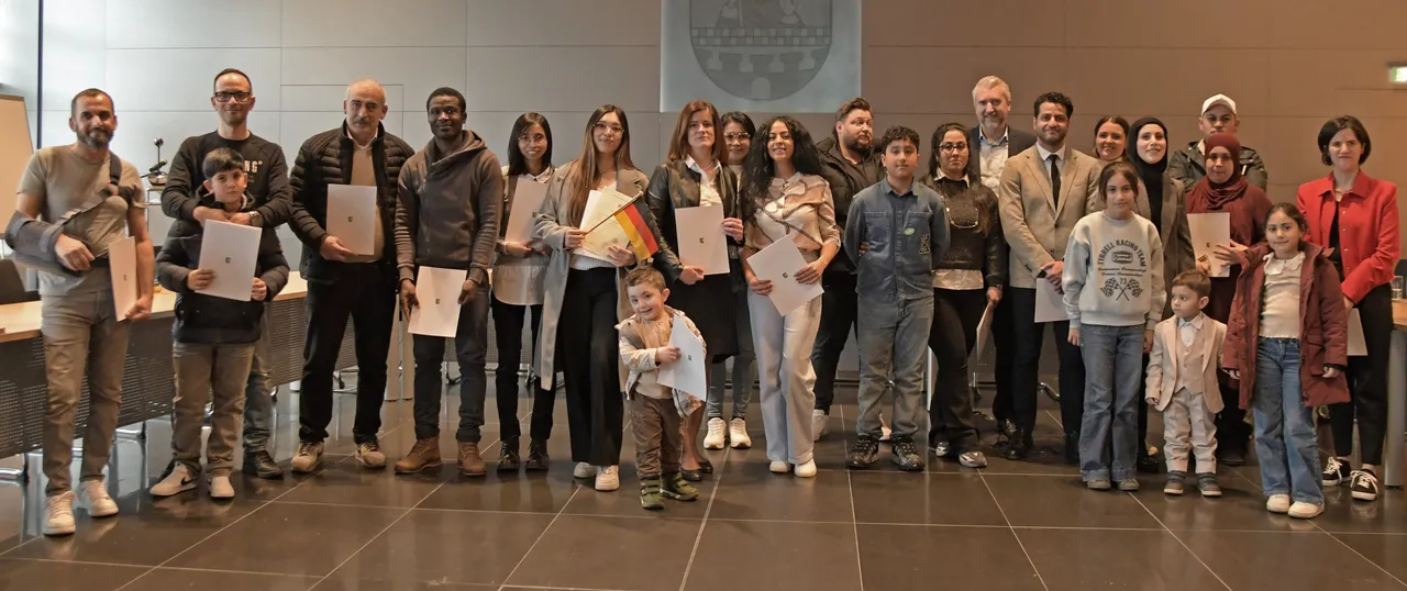 Gruppe von 42 Menschen, darunter Kinder, halten Einbürgerungsurkunden in den Händen. Im Hintergrund ist das Stadtwappen zu sehen.