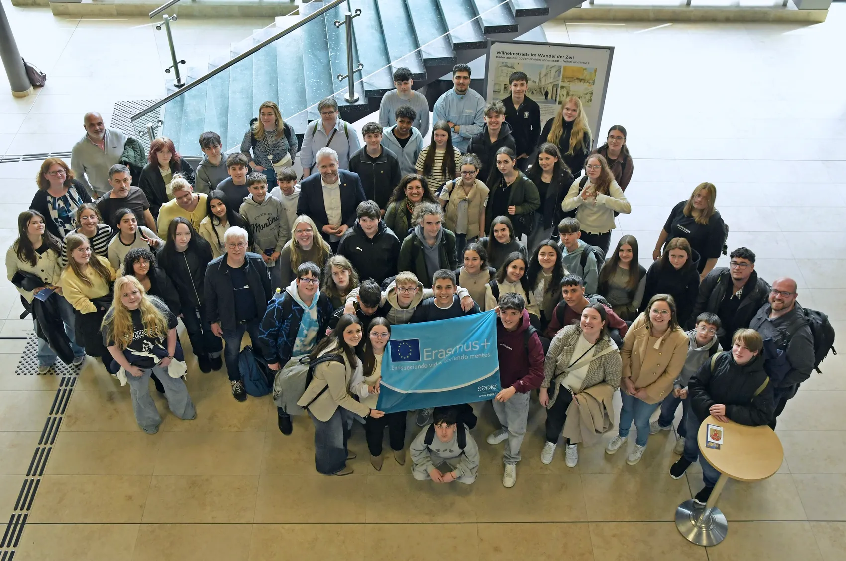 Eine Gruppe von etwa 30 Schülerinnen und Schülern aus Island, Portugal und Spanien posiert mit einem Banner mit dem Erasmus+ Logo im Rathaus. Im Hintergrund eine Treppe und eine Informationstafel.