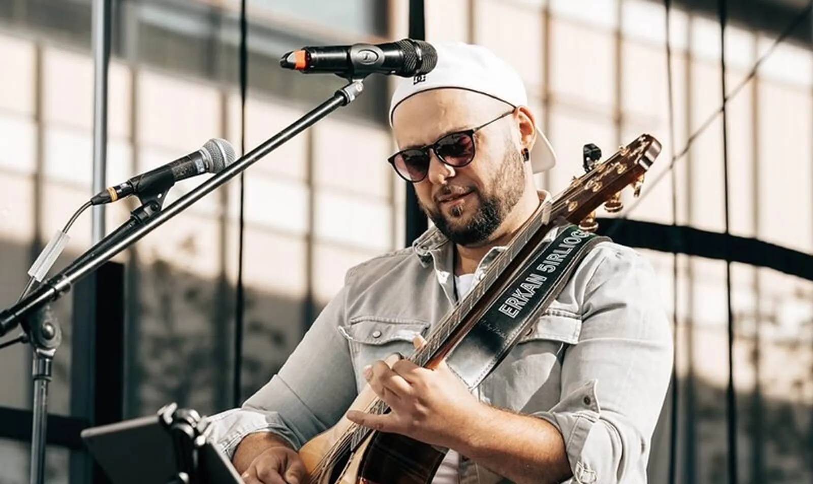 Ein Mann mit Baseballkappe und Sonnenbrille spielt Gitarre am Mikrofon auf Schloss Neuenhof.