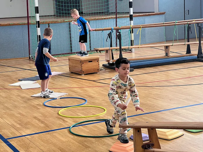 Kinder absolvieren einen Parcours in einer Turnhalle. Sie springen über Hürden und durch Reifen, während sie sich auf die Schule vorbereiten.