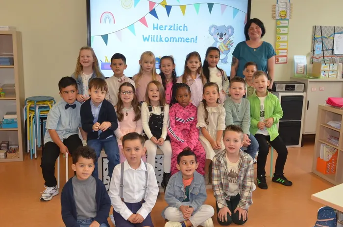 Die Klassenlehrerin Felicitas Zelic mit den Kindern der Koala-Klasse 1c vor einem Bildschirm mit der Aufschrift „Herzlich Willkommen!“.