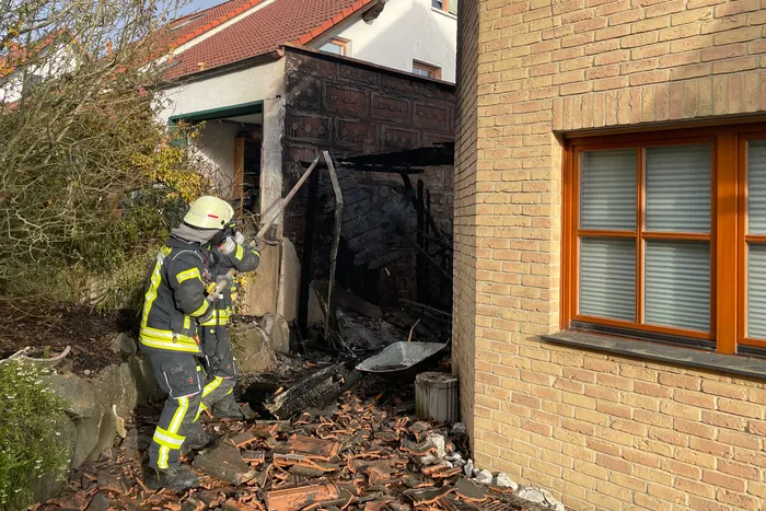 Feuerwehrleute entfernen beschädigte Fassadenteile eines Hauses nach einem Brand, um verbliebene Glutnester zu löschen.