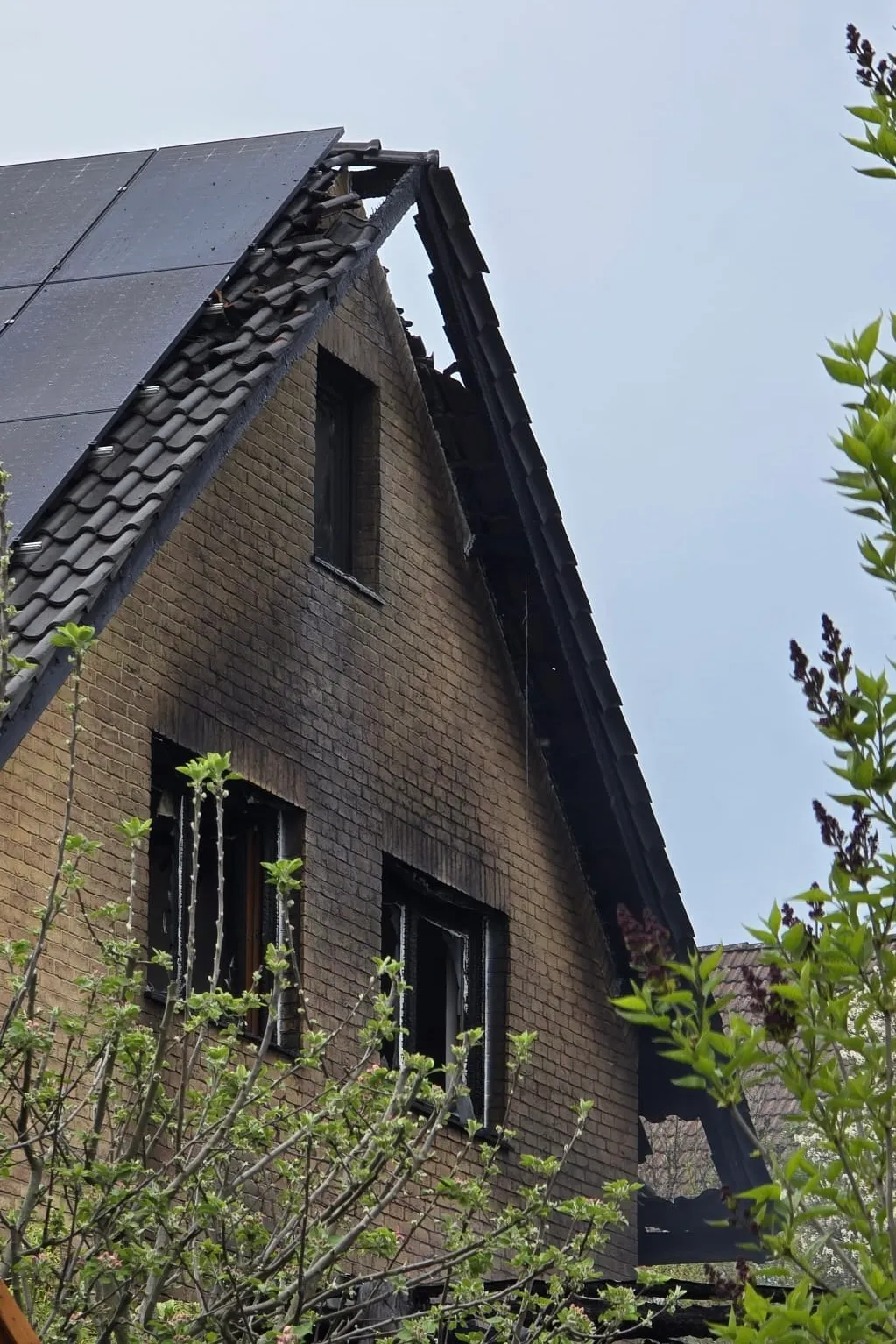 Beschädigtes Ziegeldach und ausgebrannte Fenster eines zweigeschossigen Hauses nach einem Brand.