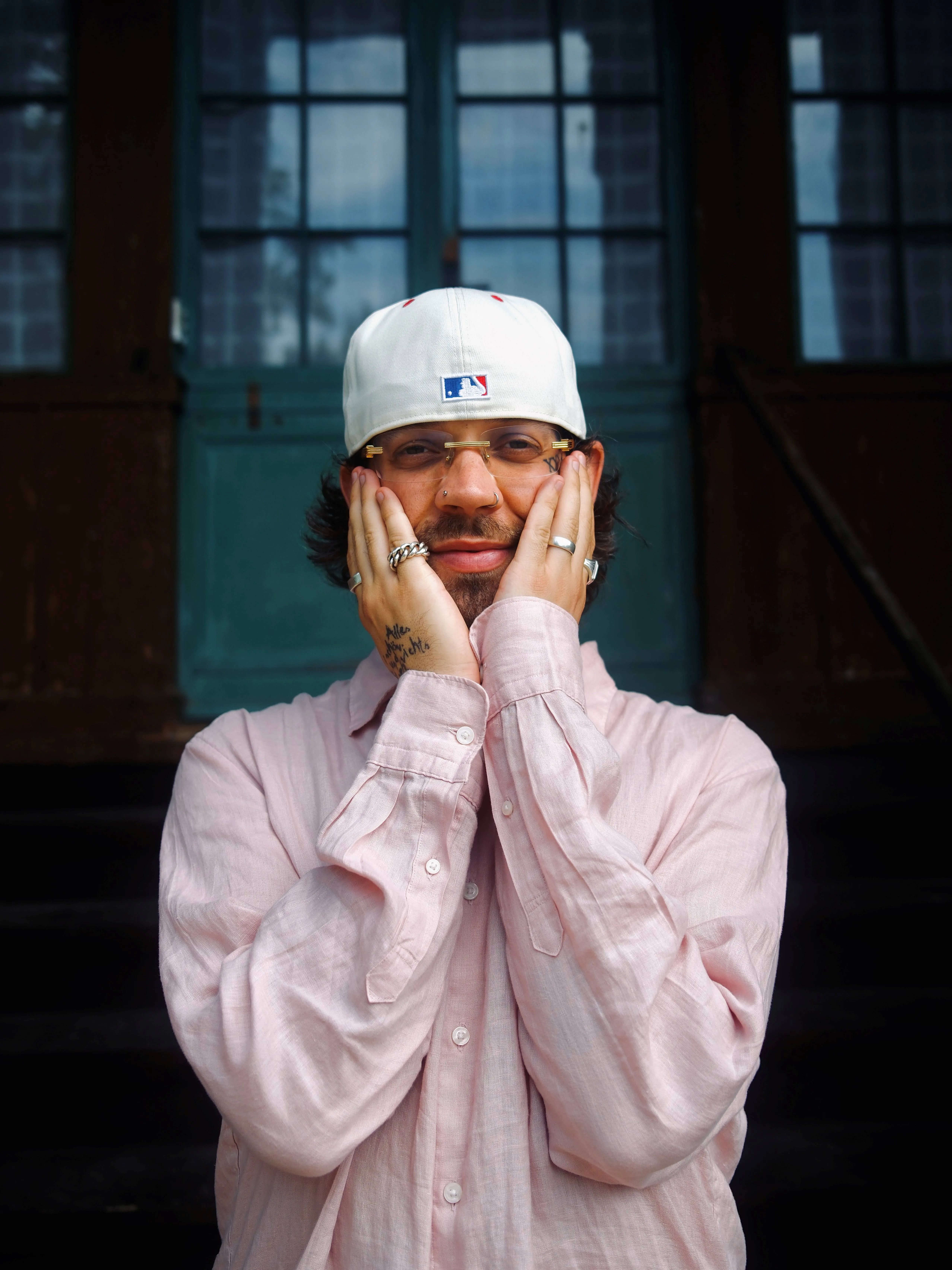 Porträt von Fayan, einem Musiker mit Bart, Brille und Baseballkappe, der sein Gesicht mit beiden Händen umrahmt.