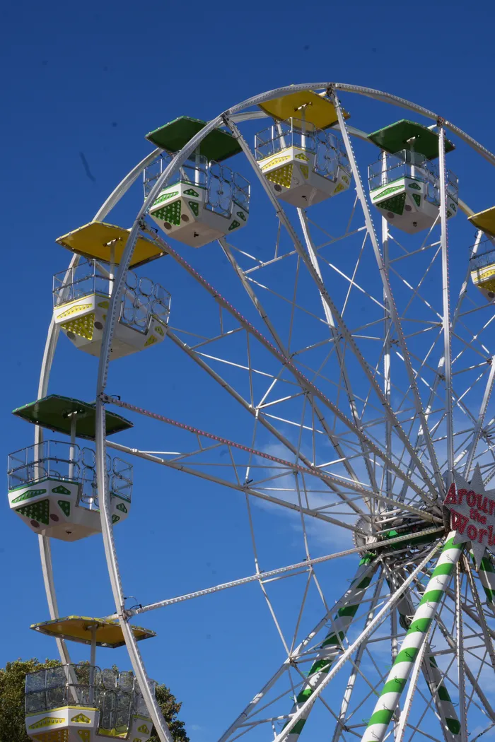 Ein weißes Riesenrad mit gelben und grünen Gondeln vor einem klaren blauen Himmel.
