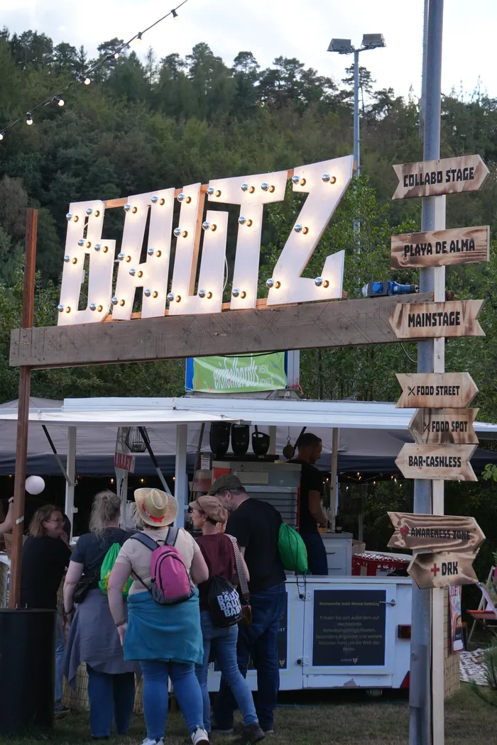 Ein großes, mit Glühbirnen beleuchtetes Holzschild mit der Aufschrift „BAUTZ“ und hölzerne Wegweiser zu verschiedenen Festivalbereichen.
