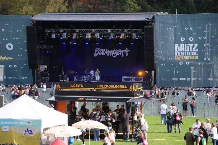Beleuchtete Bühne mit der Aufschrift „Baumgart“ und ein Imbissstand vor einer Menschenmenge beim Bautz Festival.