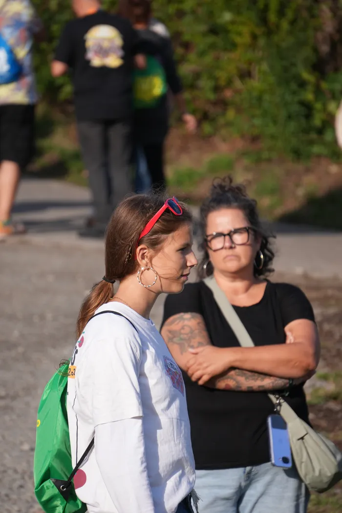 Eine junge Frau mit weißem T-Shirt und grünem Rucksack steht neben einer Frau mit Brille und Tattoos auf einem Weg beim Bautz 2026.