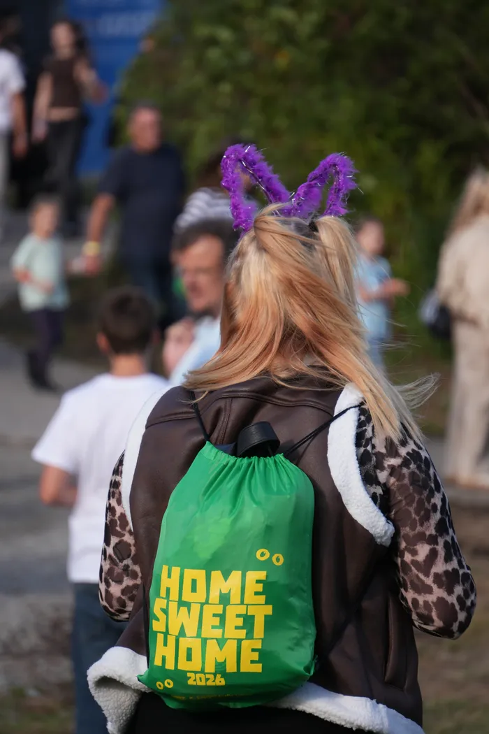 Eine Person mit lila Hasenohren trägt einen grünen Beutel mit der gelben Aufschrift „HOME SWEET HOME 2026“.
