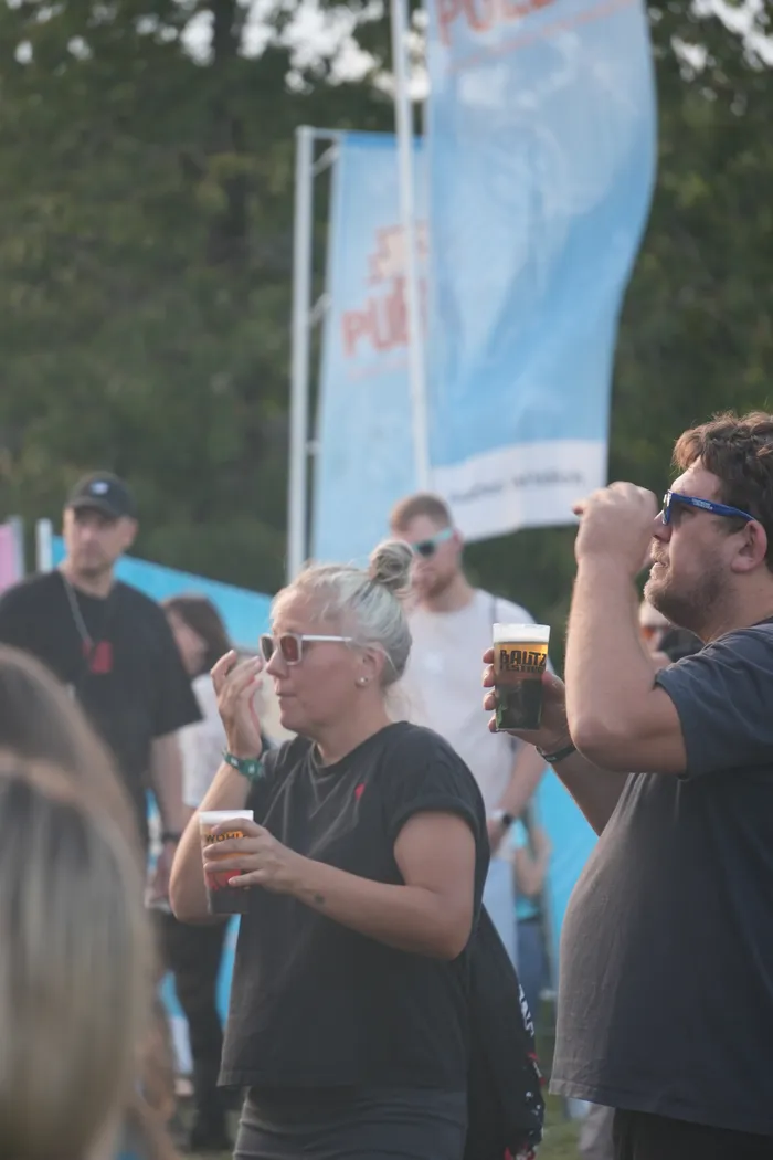 Besucher mit Getränken in den Händen feiern vor blauen Fahnen bei dem Bautz 2026 Festival.