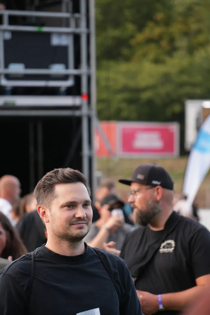 Ein lächelnder Mann im schwarzen T-Shirt blickt in eine Menschenmenge vor einer großen Bühne.