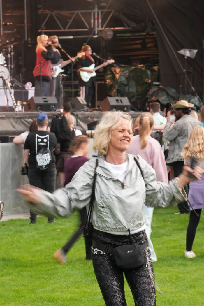 Eine Frau tanzt mit ausgebreiteten Armen vor einer Bühne, auf der eine Band spielt.