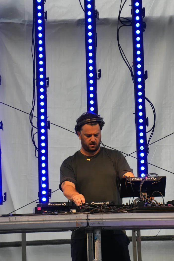 Der DJ Knallblech bedient sein Mischpult vor drei vertikalen blauen LED-Lichtstreifen.