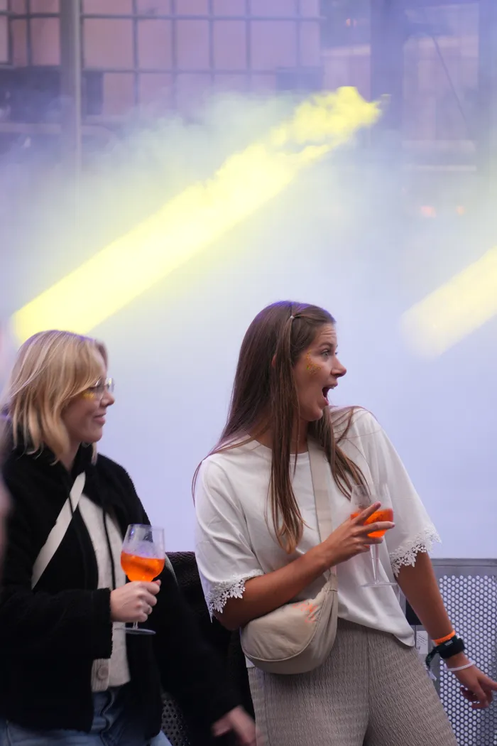 Eine junge Frau mit weit geöffnetem Mund blickt begeistert bei einem Konzert auf das Bautz 2026, während gelbe Lichtstrahlen durch Nebel scheinen.