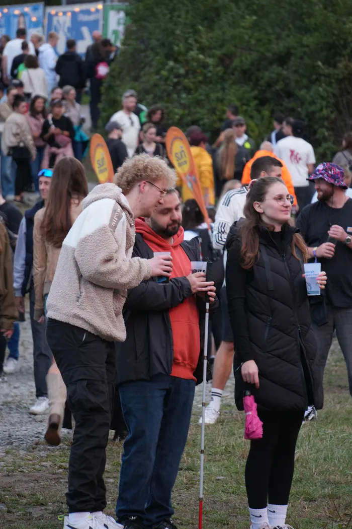 Junge Menschen stehen mit Getränken in einer Menschenmenge bei einem Open-Air-Festival.