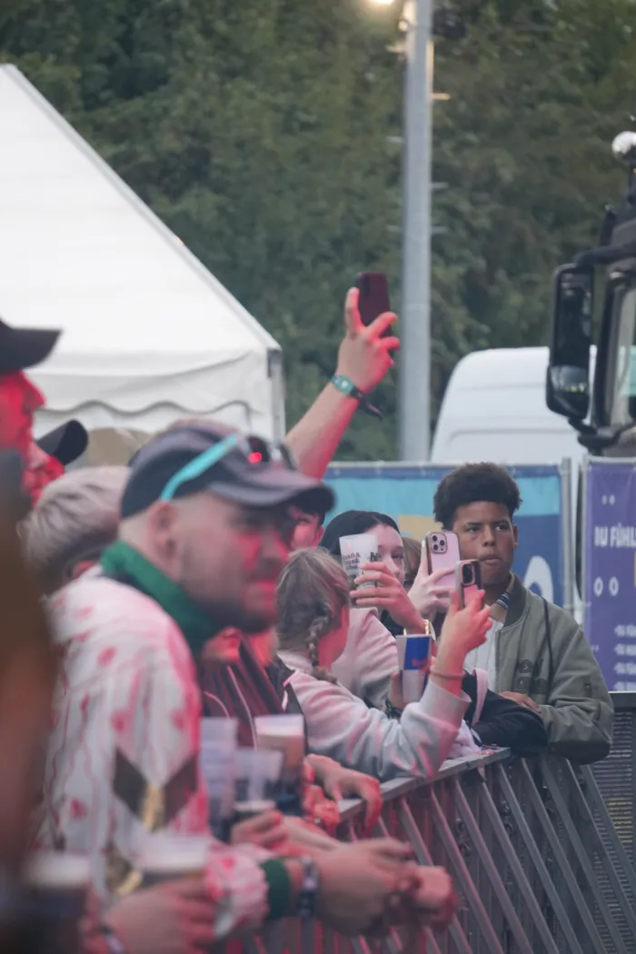 Publikum bei einem Festival hält Getränke und Smartphones hoch, um eine Performance zu verfolgen.