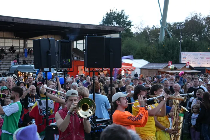 Musiker spielen Blasinstrumente inmitten einer großen Menschenmenge bei einem Open-Air-Event.