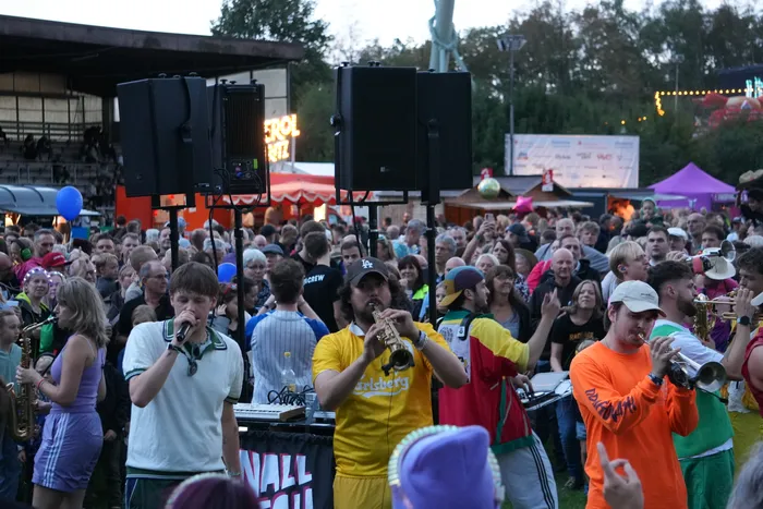 Musiker der Band Knallblech spielen Blasinstrumente und singen inmitten einer großen Menschenmenge bei einem Open-Air-Festival.